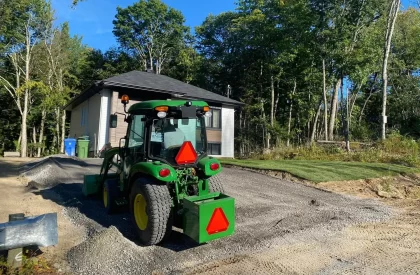 Homme épandant du gravier avec un tracteur pour agrandir un stationnement