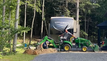 "Homme sur tracteur chargeur creusant une tranchée pour installation de drain dans un aménagement paysager"