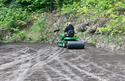 Un homme sur un tracteur muni d’un rouleau compresseur nivelant le sol